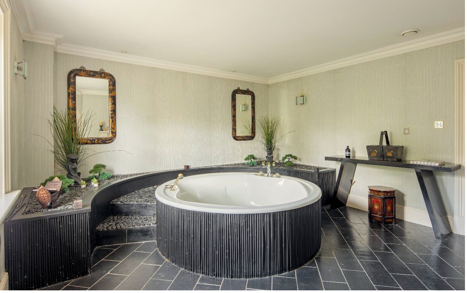 A modern bathroom with a freestanding bathtub, two wall mirrors, and a small table with decorative items.