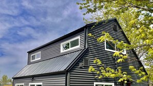 A two-story house with a dark exterior, multiple windows, and a small front yard with a tree. - Carriage house! Close to hospital, firepit, outdoor dining (lima)