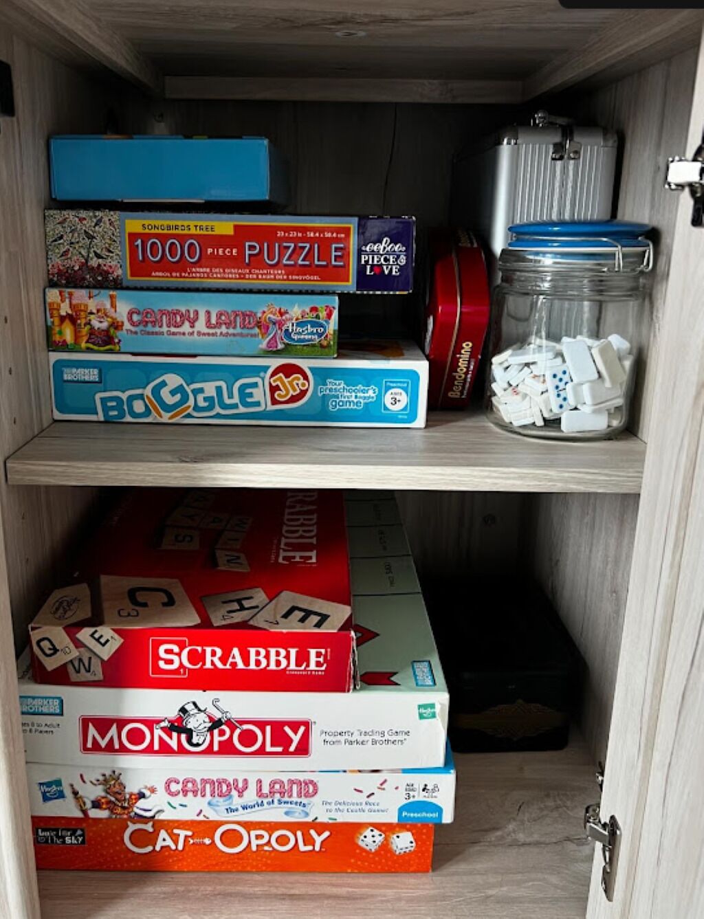Uma estante com vários jogos de tabuleiro, incluindo Scrabble, Monopoly, Candy Land e outros.