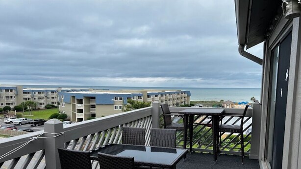 A balcony with outdoor seating, overlooking a beach and adjacent buildings. - Beautiful 2-bedroom condo with ocean views, Wi-Fi, AC, wshr/dryr in Myrtle Beach (Myrtle Beach)