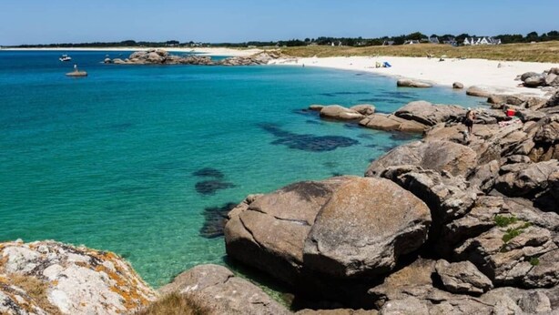 A coastal beach with clear turquoise water, large rocks, and a sandy shore.
