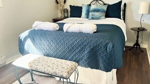 Ein ordentlich bezogenes Bett mit einer blauen Steude, weißen Kissen und einem Nachttisch mit einer Lampe.