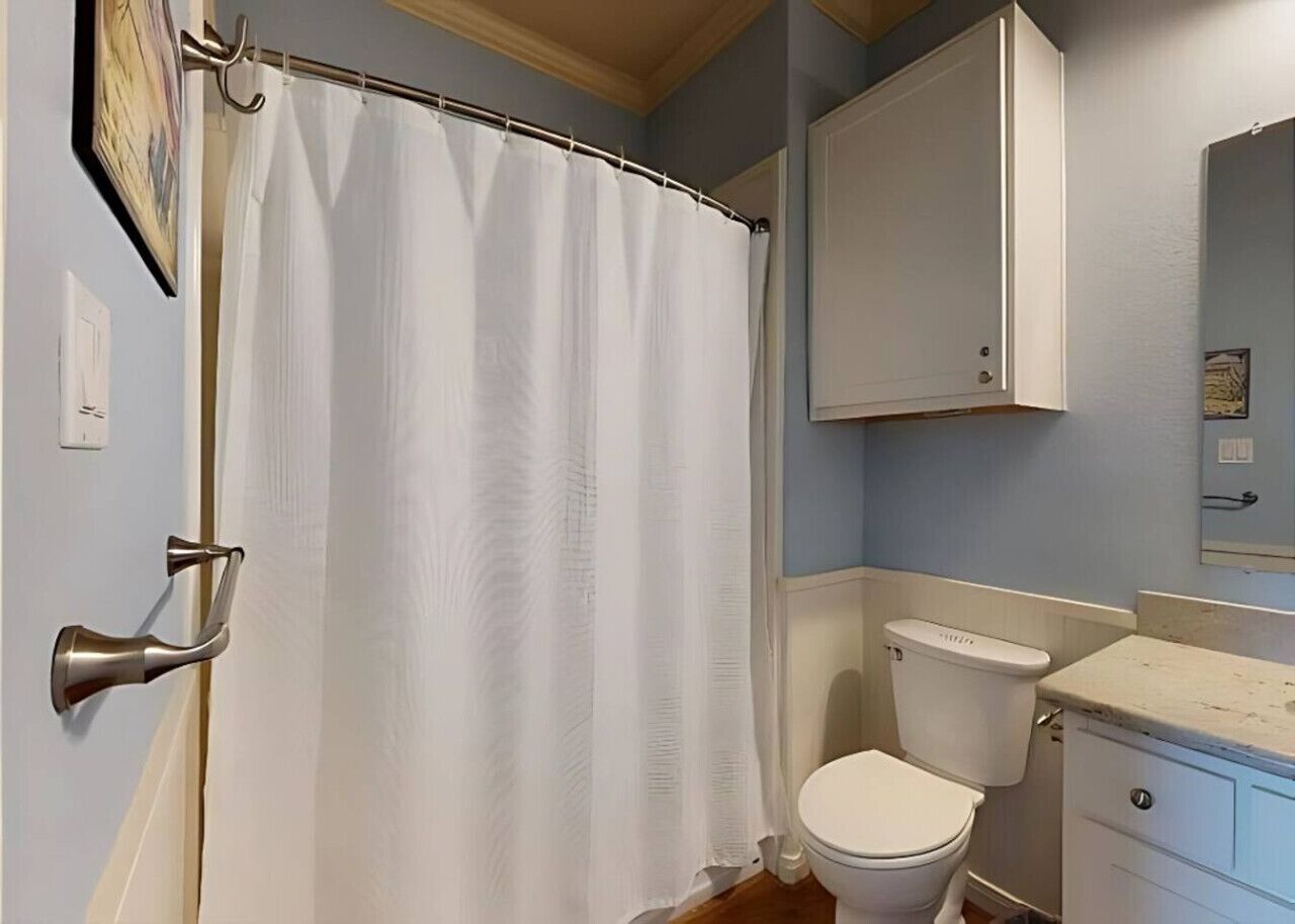 Un baño con cortina de ducha, inodoro, lavamanos y un armario.