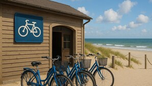 A wooden building with a bicycle sign, a beach view, and several bicycles with baskets. - Jonte's Nest  (Wurster Nordseeküste)