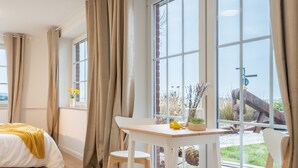 A bedroom with a bed, a small table, and a window with curtains. - Jonte's Nest  (Wurster Nordseeküste)
