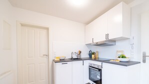 A compact kitchen with white cabinetry, a built-in oven, and a countertop with a bowl and utensils. - Jonte's Nest  (Wurster Nordseeküste)