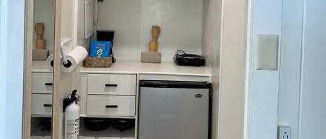 A compact kitchenette with a microwave, refrigerator, and various kitchen utensils.