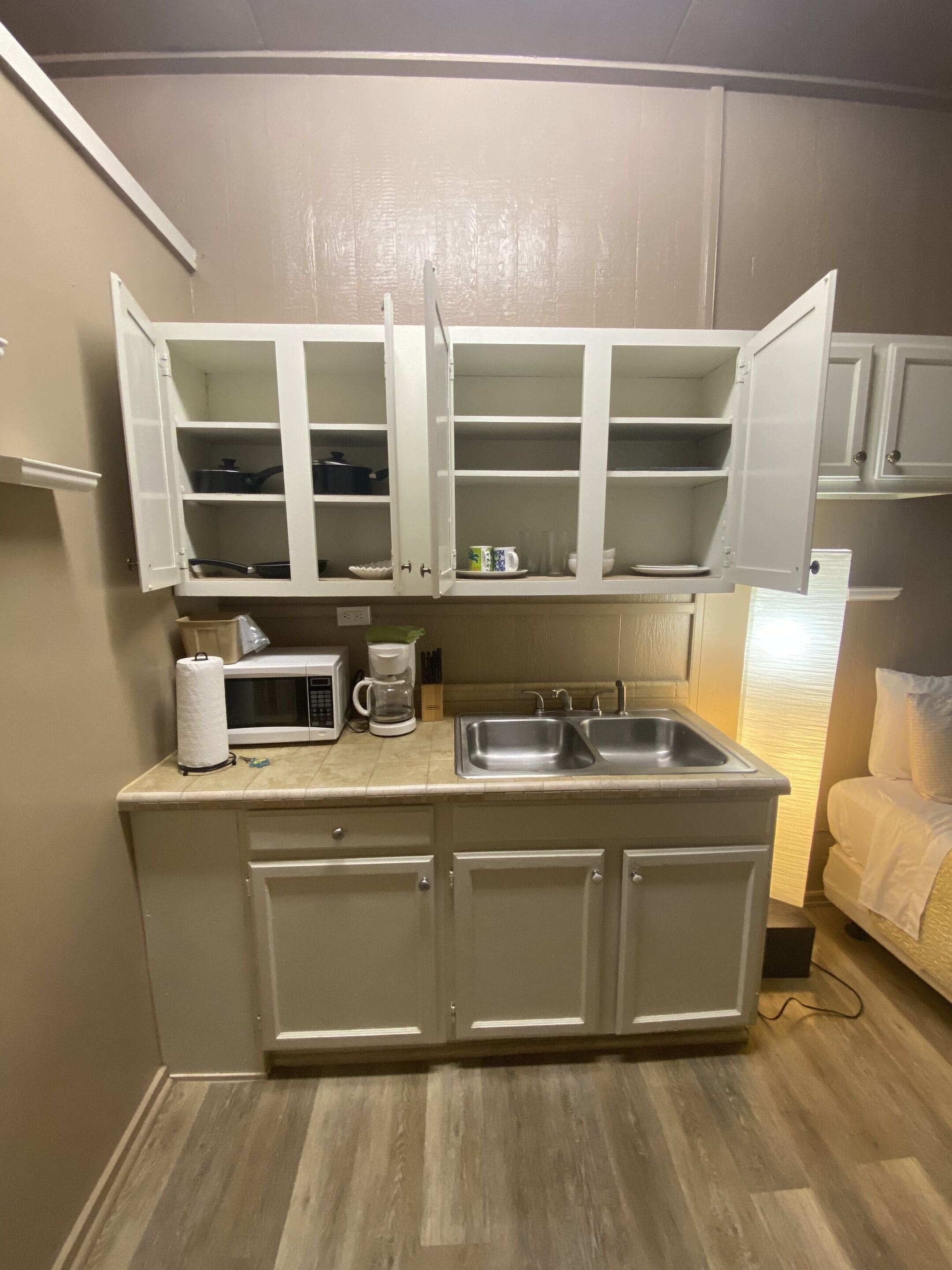 A compact kitchenette with a microwave, coffee maker, and two open cabinets above a sink.