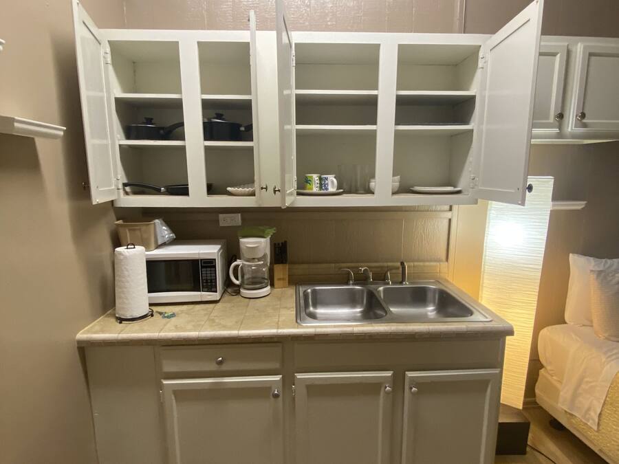 Una kitchenette compacta con microondas, cafetera y dos alacenas abiertas sobre un lavamanos.