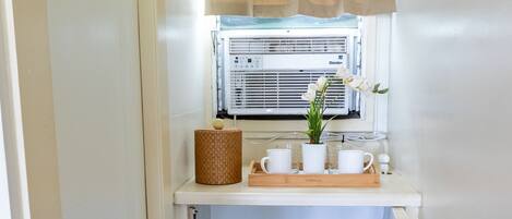 Una kitchenette compacta con un refrigerador pequeño, una ventana con cortina y una planta en maceta sobre la encimera.