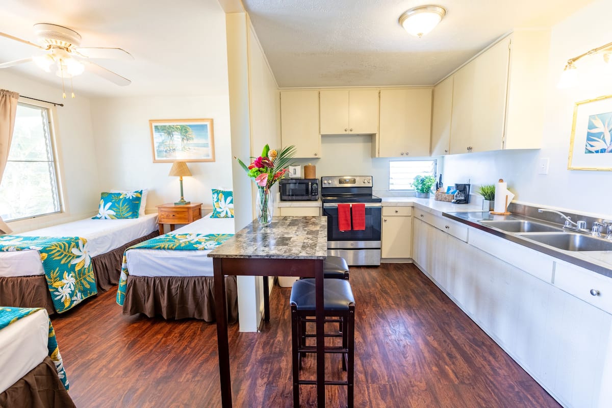 Cocina compacta con una isla central, comedor con mesa y sillas, y un dormitorio con dos camas.