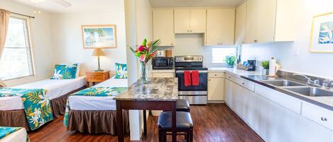 A compact kitchen with a central island, a dining area with a table and chairs, and a bedroom with two beds.