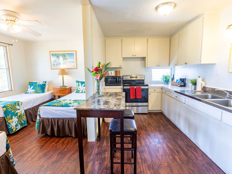 A compact kitchen with a central island, a dining area with a table and chairs, and a bedroom with two beds.