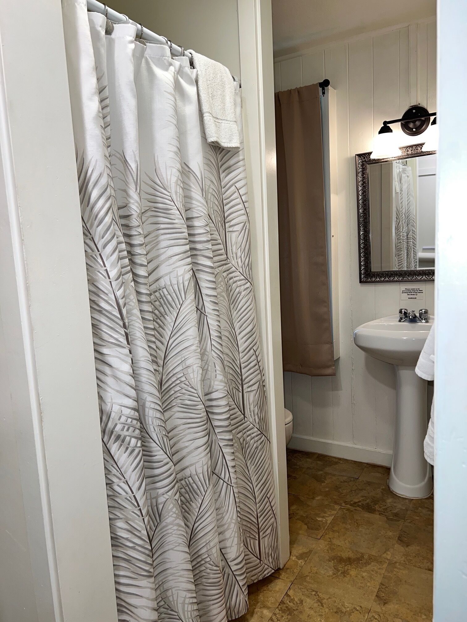 A bathroom with a shower curtain featuring a leaf pattern, a sink, and a mirror with a decorative frame.