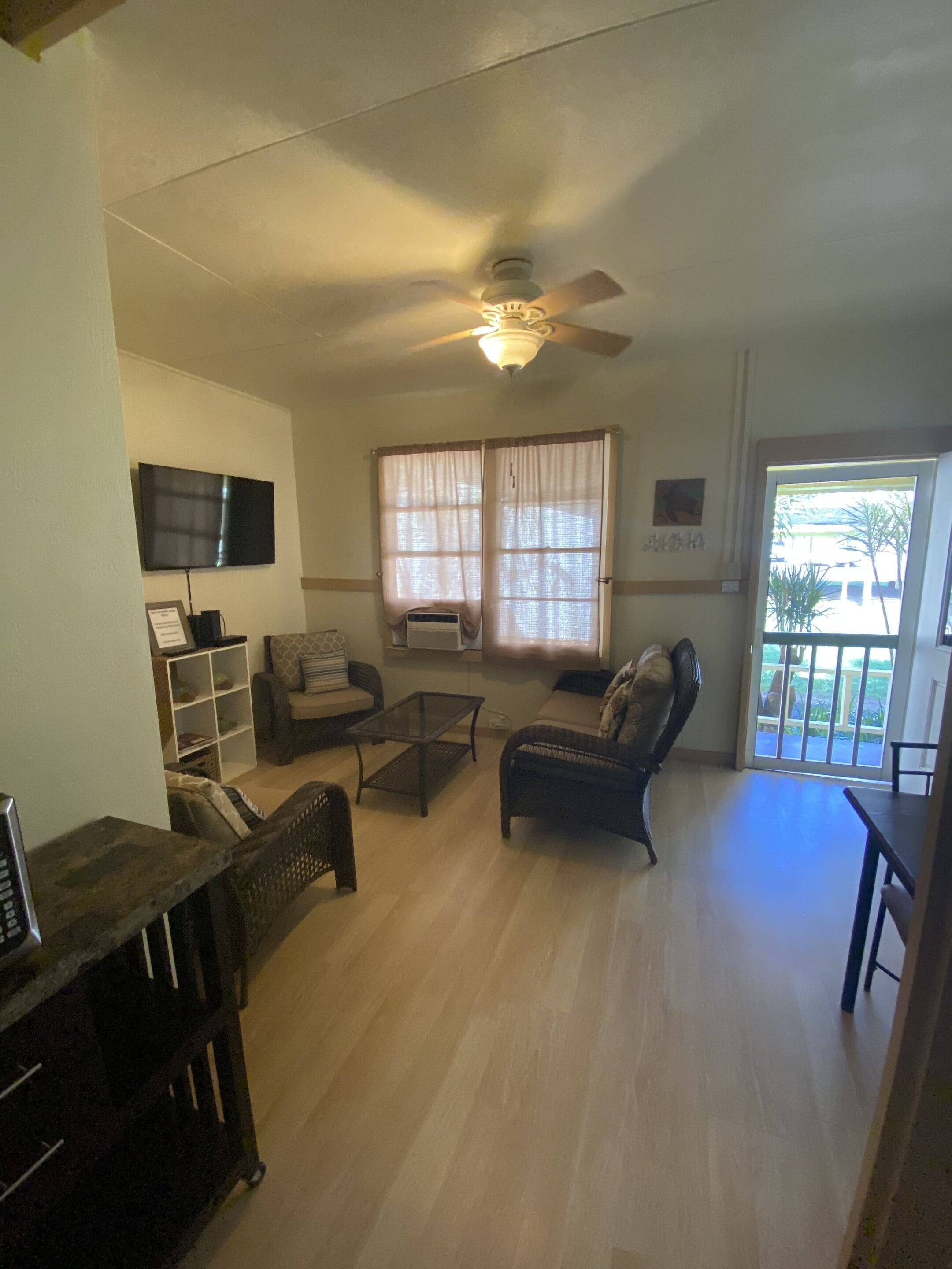 Un salon avec un ventilateur de plafond, un téléviseur, un canapé, une table basse et une fenêtre avec des rideaux.