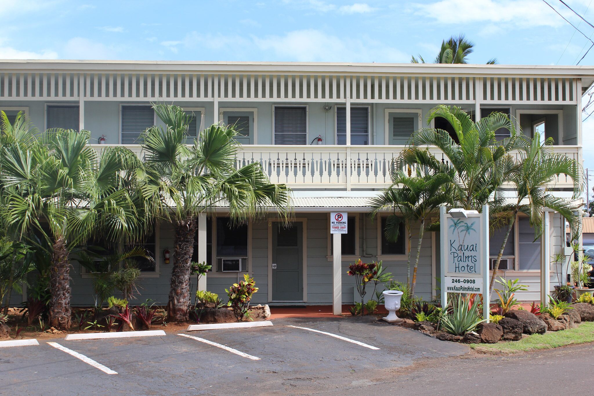 Ein zweistöckiges Gebäude mit einer Veranda, Palmen und einem Schild für das Kauai Palms Hotel.