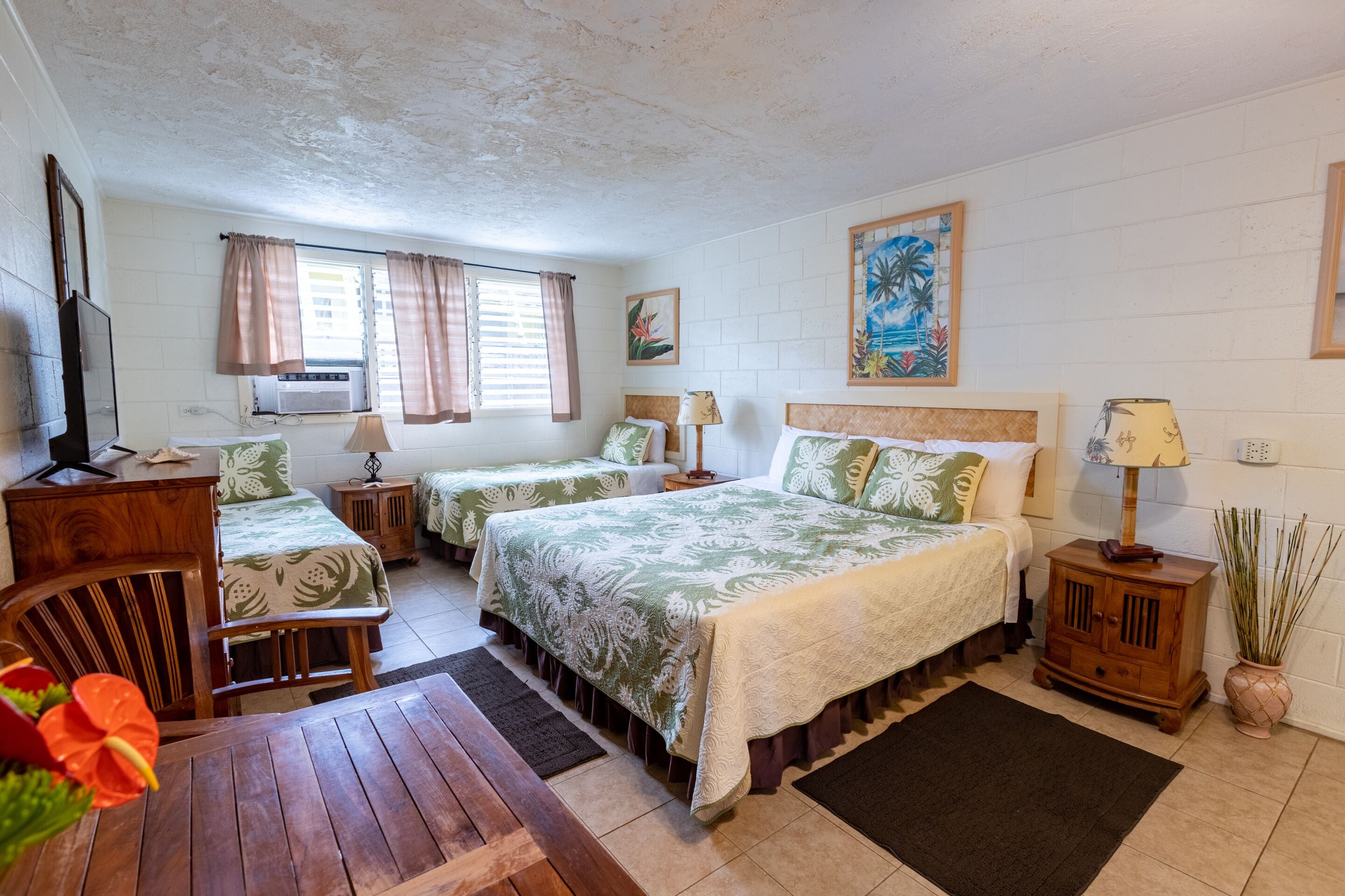 A hotel room with two single beds, a wooden desk, a television, and a window with curtains.