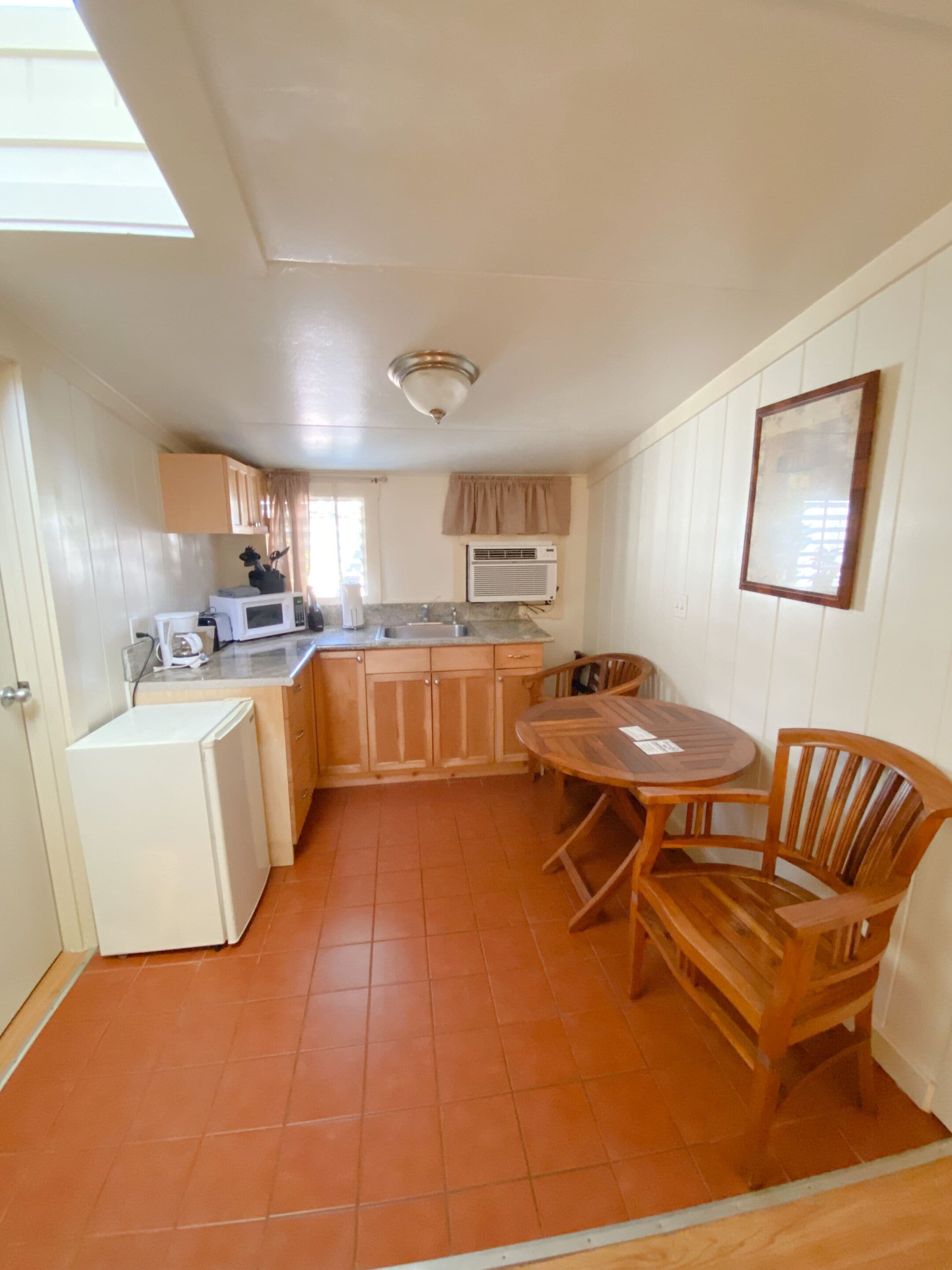 Una cocina compacta con refrigerador, microondas, lavamanos y armarios de madera.