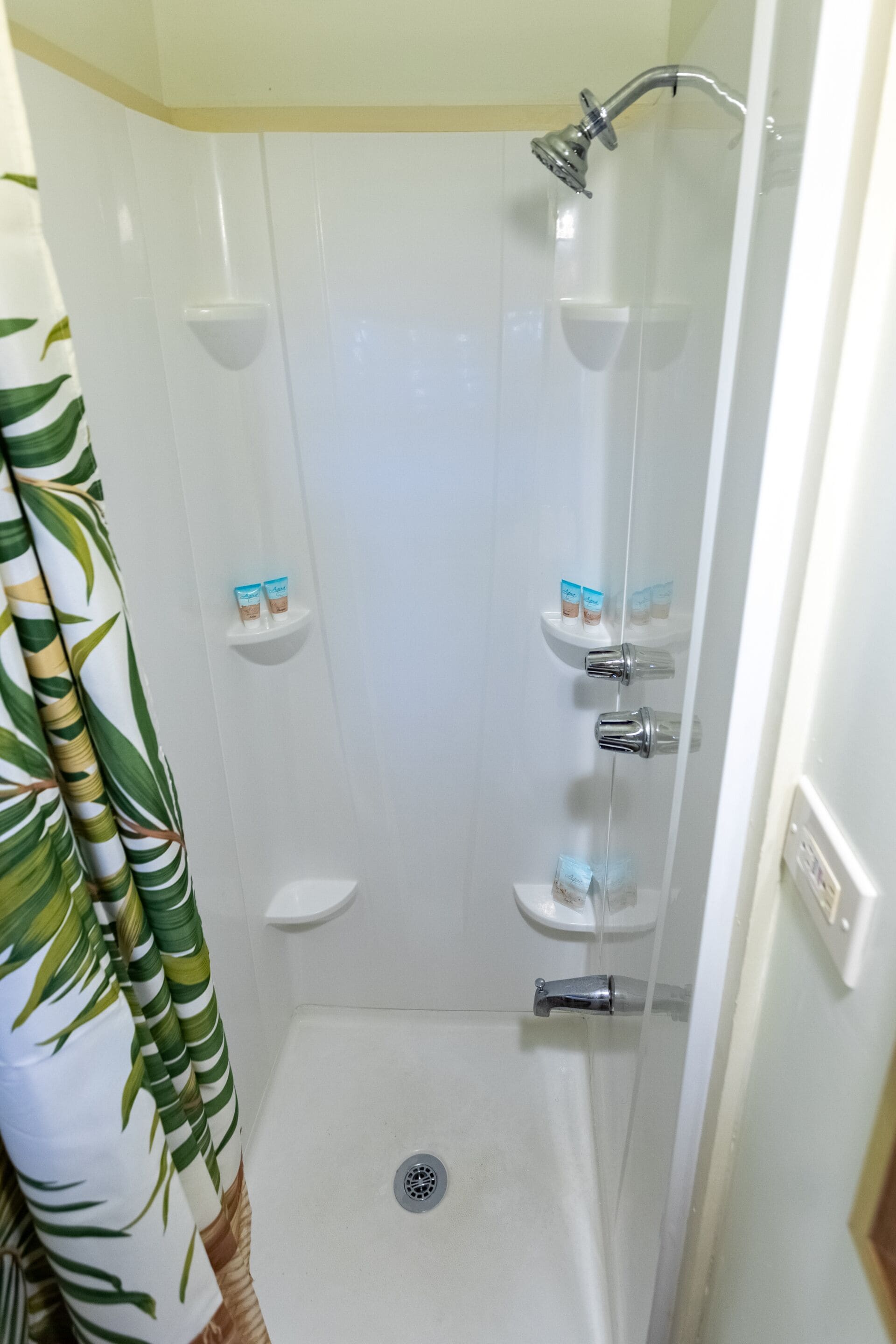 Una doccia con porta in vetro, uno scaffale con articoli da toilette e uno scarico.