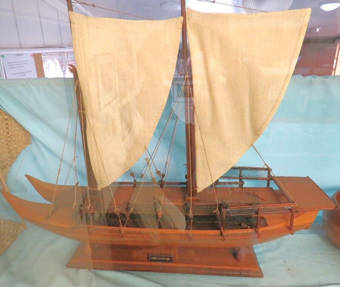 A model ship with a wooden hull and two sails, displayed on a stand.