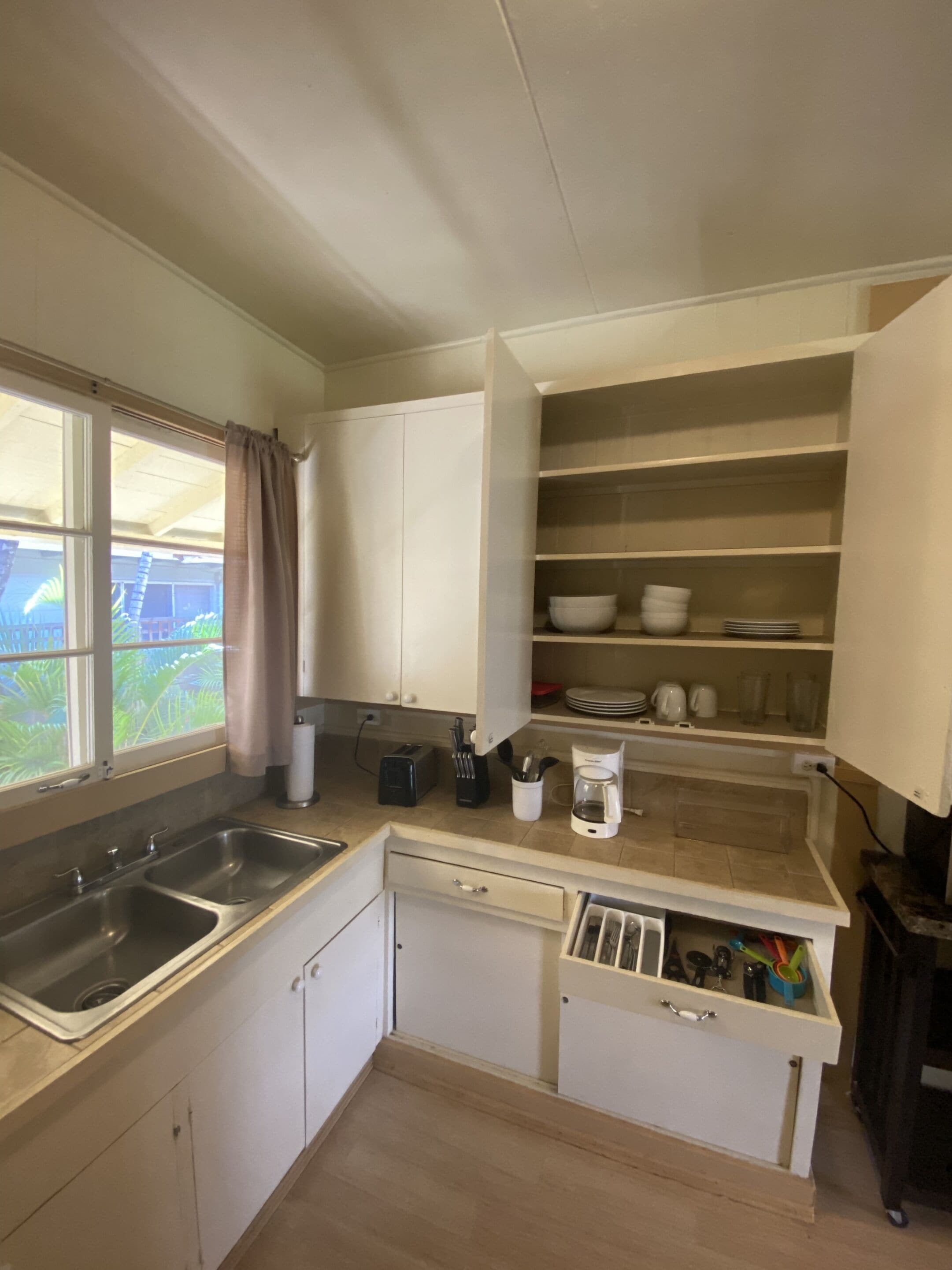 A compact kitchen with a double sink, white cabinets, and a window with a view of greenery.
