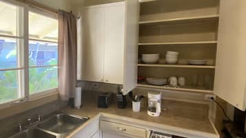 A compact kitchen with a double sink, white cabinets, and a window with a view of greenery.