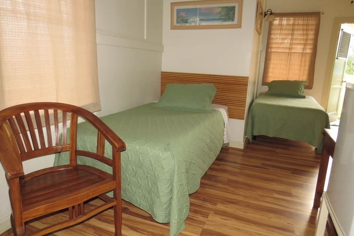 Una habitación con dos camas, una silla de madera y un cuadro en la pared.