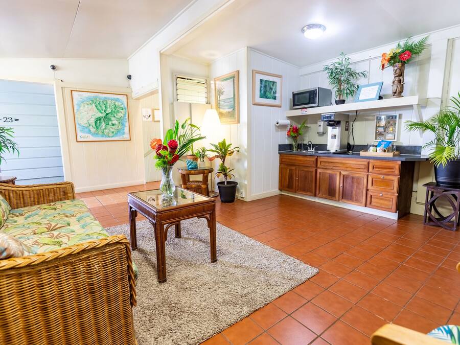 A cozy living room with a wicker sofa, a glass-top coffee table, and a kitchen area with wooden cabinets and a microwave.