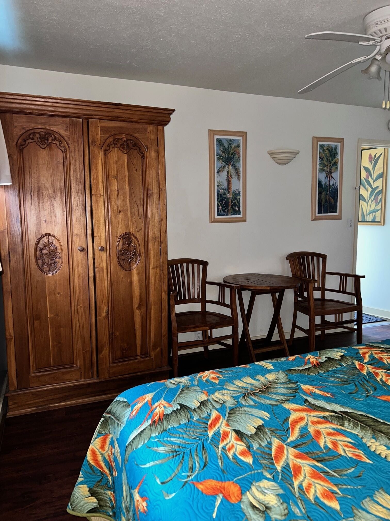 Una habitación con un armario de madera, una mesa de comedor con sillas y una cama con colcha estampada.