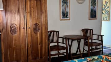 Una habitación con un armario de madera, una mesa de comedor con sillas y una cama con colcha estampada.