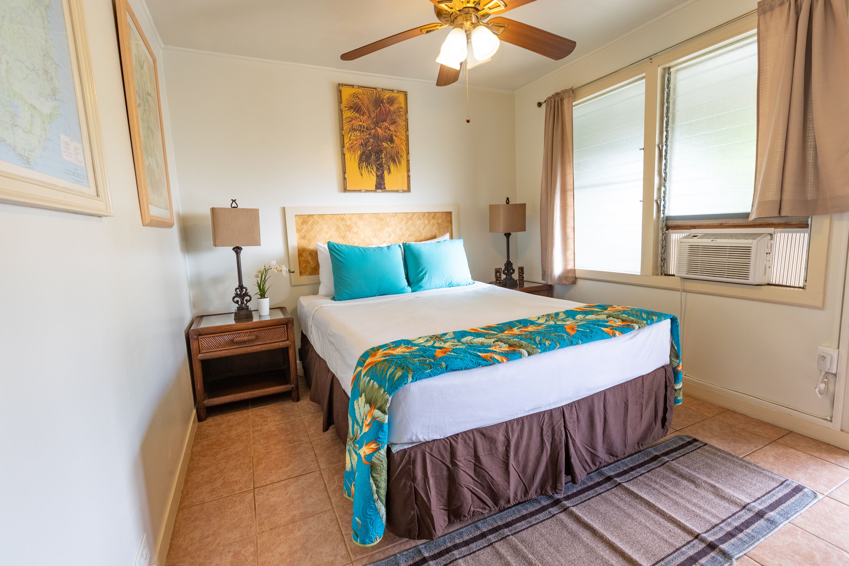 A bedroom with a bed, two bedside tables, a ceiling fan, a window with curtains, and a wall-mounted air conditioner.
