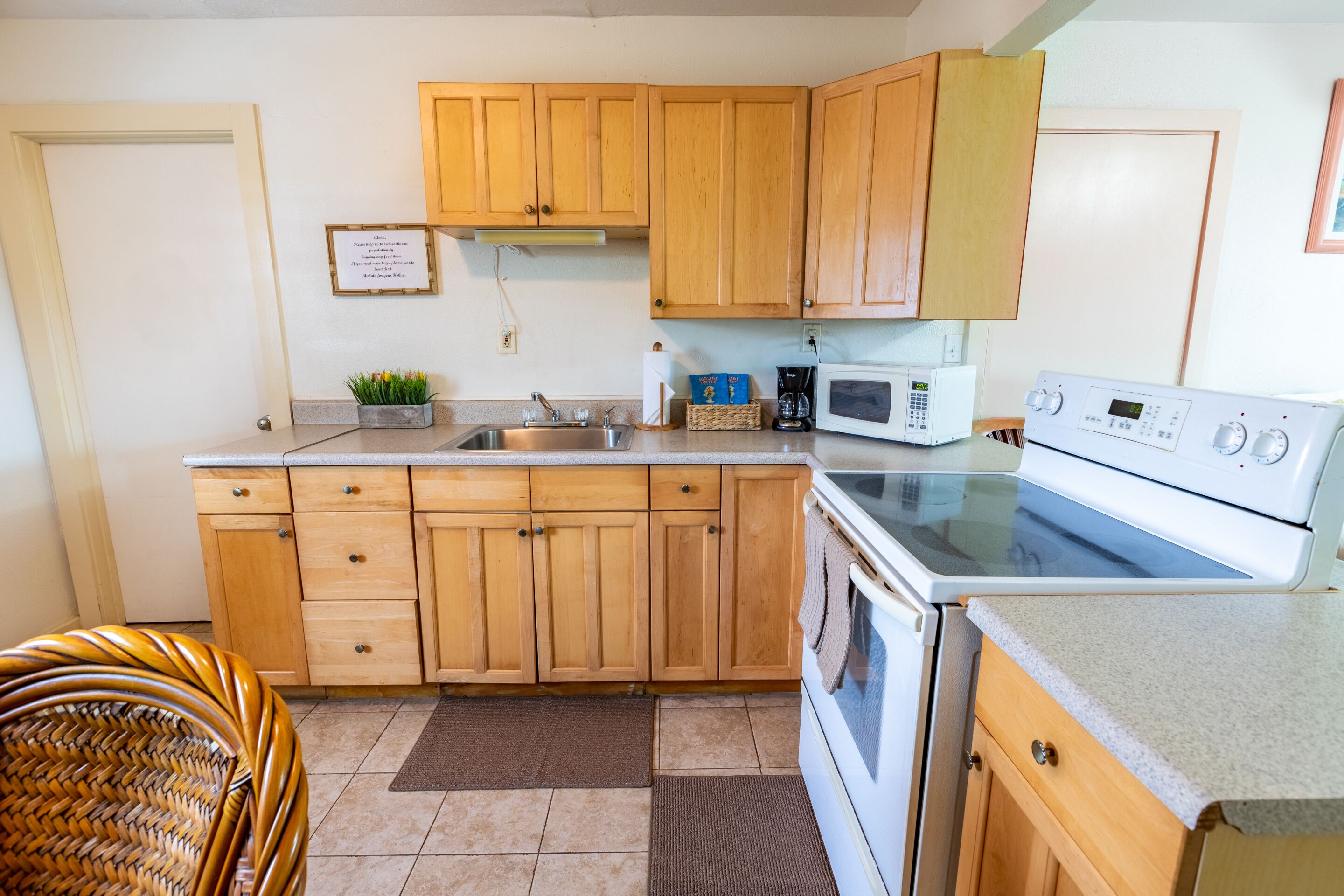 Une cuisine avec des meubles de rangement en bois, un four à micro-ondes, une cuisinière et une chaise en osier.
