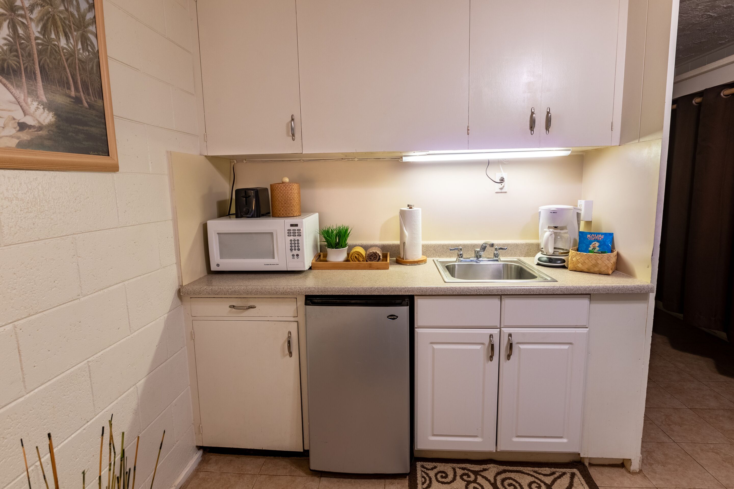 A compact kitchen with white cabinets, a microwave, a coffee maker, and a sink.