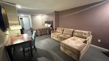 A hotel room with a bed, a sofa, a desk with a chair, and a mirror.