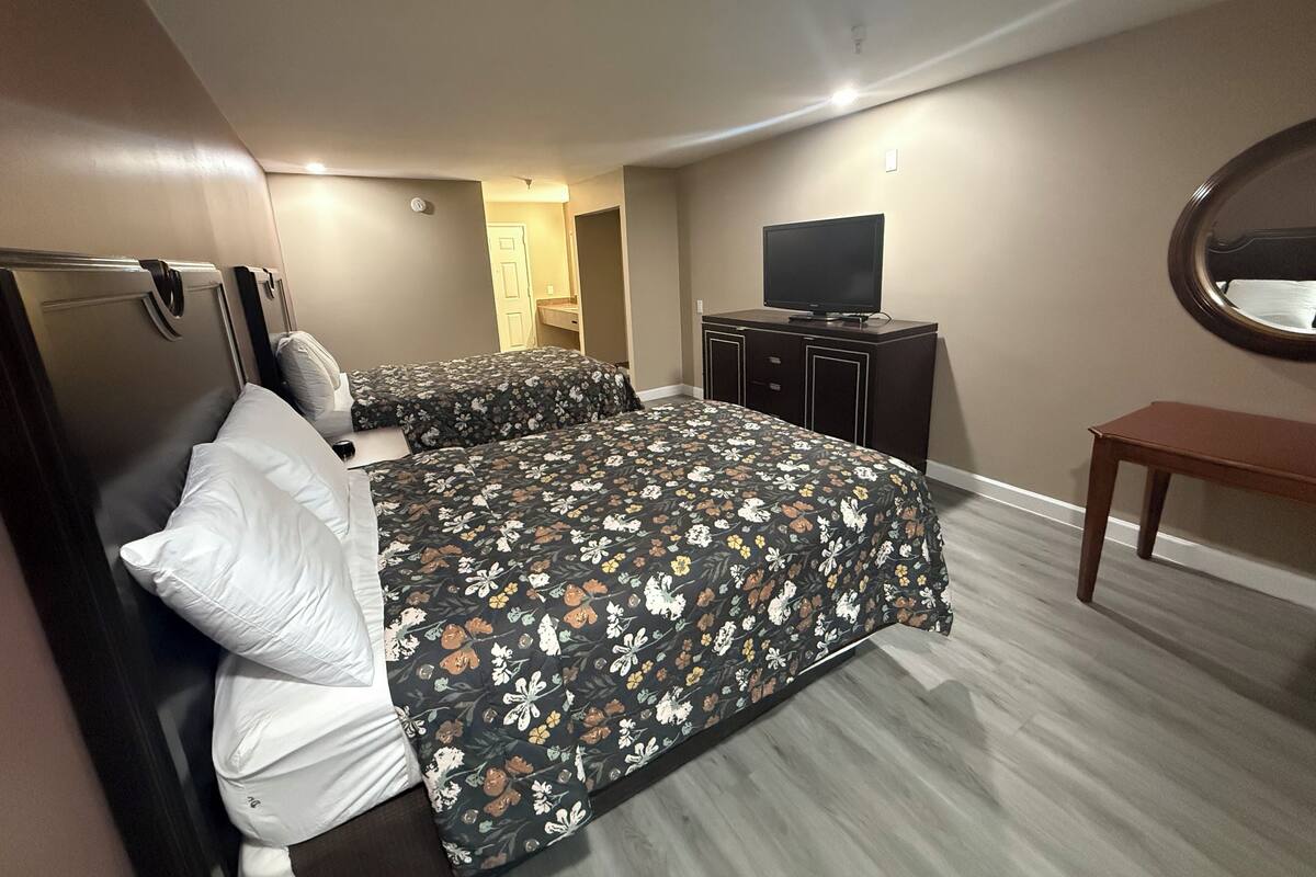A hotel room with two beds, a television, a small table, and a mirror on the wall.