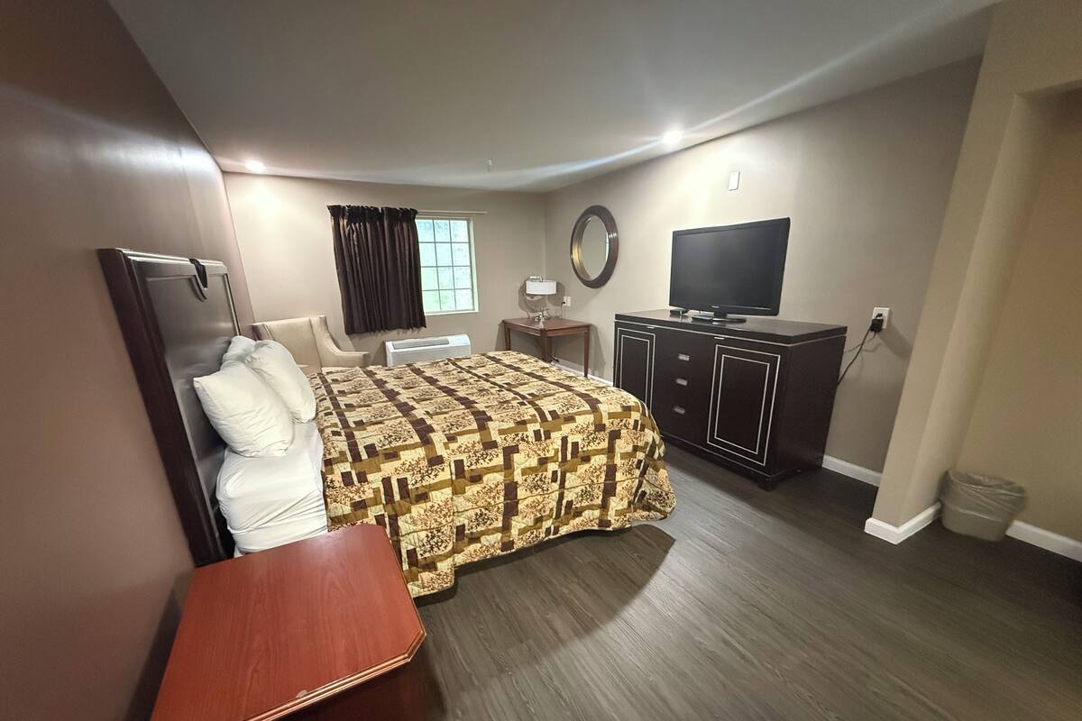 A bedroom with a bed, a desk, a TV, and a dresser.