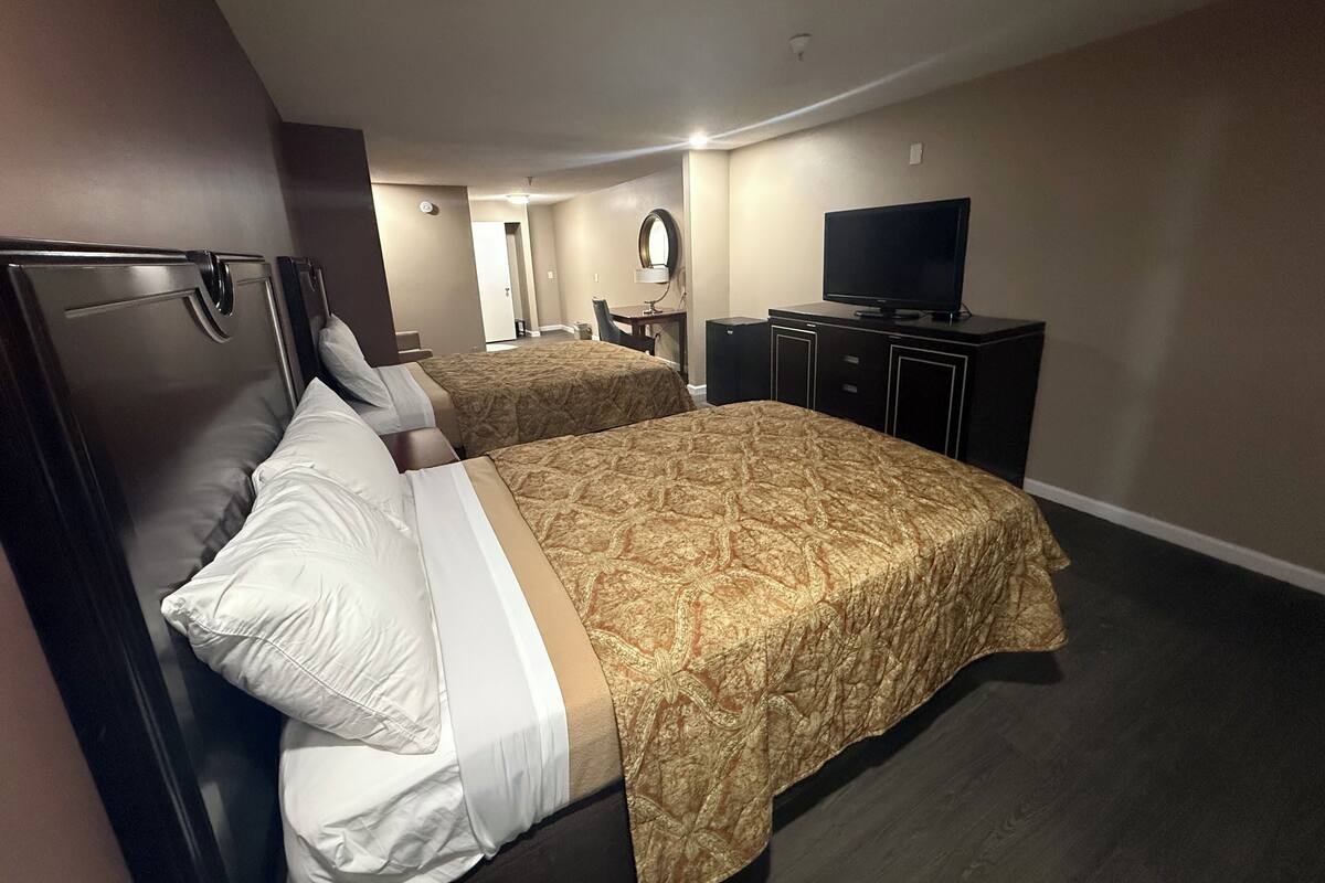 A hotel room with two beds, a TV, a desk, and a mirror.