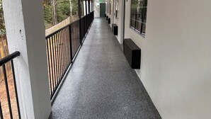 Un pasillo cubierto con barandilla negra, suelo de concreto y ventanas a un lado.