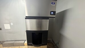 Un dispensador de agua de acero inoxidable con pantalla digital, fijado a una pared con suelo de baldosas.
