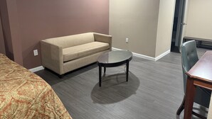 Una habitación de hotel con un sofá color beige, una mesita redonda pequeña y una silla de madera.