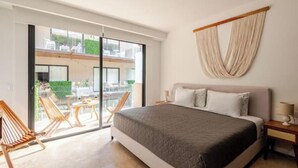 Quarto com cama, mesa de cabeceira, cadeira e vista através de uma porta de vidro deslizante para uma área externa com móveis.