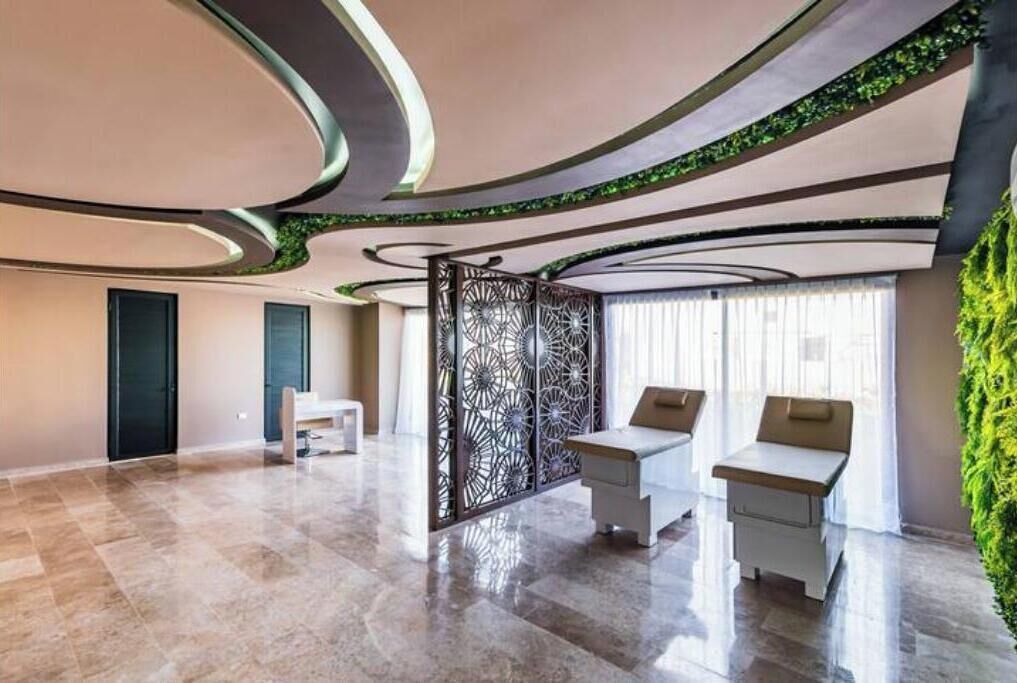 Una habitación amplia con techo curvo, un separador decorativo y un área de descanso con dos sillones.