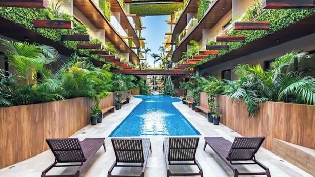 Um átrio moderno de hotel com piscina central, rodeado por vegetação exuberante e painéis de madeira.