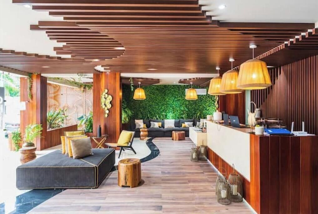 Et moderne receptionsområde med en træreception, en sofa og en grøn væg med planter.