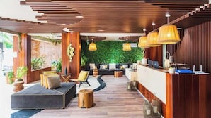 A modern reception area with a wooden reception desk, a sofa, and a green wall with plants. - Tulum City Apartments M-228 (Tulum)