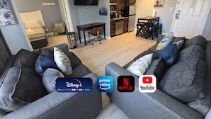 Una sala de estar moderna con sofás grises, televisor, cocina y comedor.