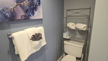A bathroom with a toilet, a metal towel rack, a wall-mounted towel dispenser, and a large abstract painting.