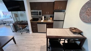 Una cocina compacta con electrodomésticos modernos, un comedor con mesa y sillas, y una pequeña zona de trabajo con escritorio y silla.