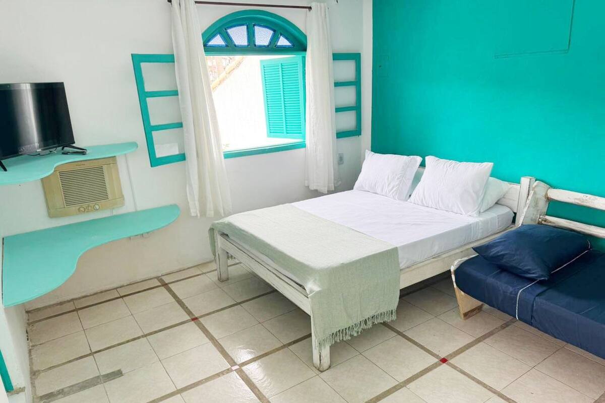 Ein Zimmer mit einem Bett, einem Fernseher, einem Fenster mit Vorhängen und einer türkisblauen Wand.