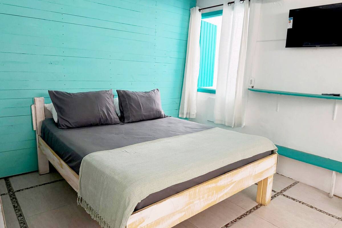Ein Bett mit einer grau-weißen Decke, zwei grauen Kissen und einer hellgrünen Tagesdecke.
